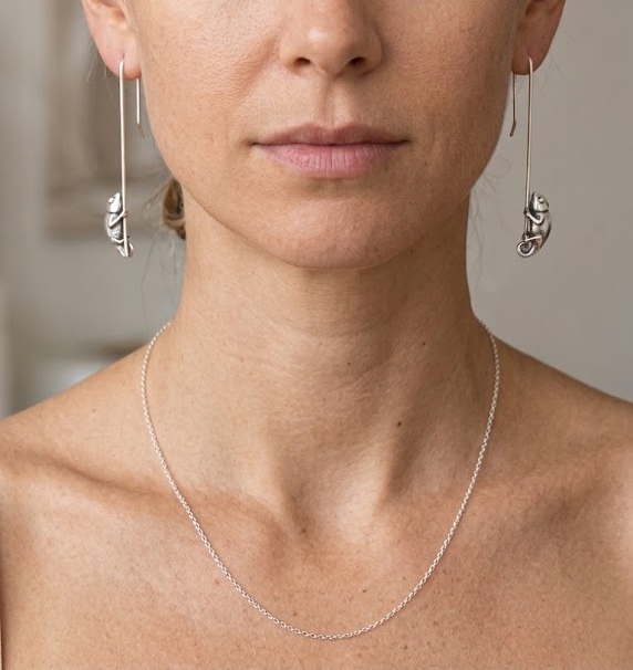 Woman wearing long silver wire drop earrings with detailed silver chameleon charms hanging on long drops, front view.