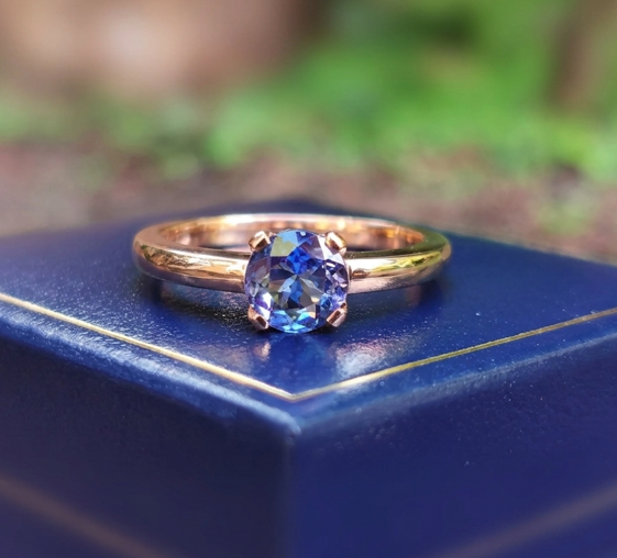 Solitaire 9ct rose gold tanzanite engagement ring resting on a blue velvet presentation box, featuring a brilliant deep blue-violet oval tanzanite gemstone.