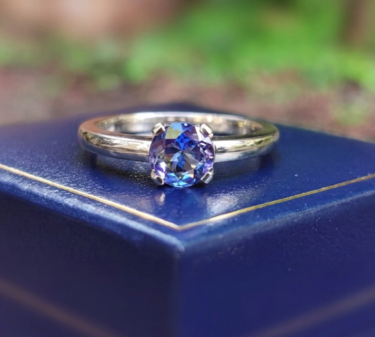 Solitaire 9ct white gold tanzanite engagement ring resting on a blue velvet presentation box, featuring a brilliant deep blue-violet oval tanzanite gemstone.