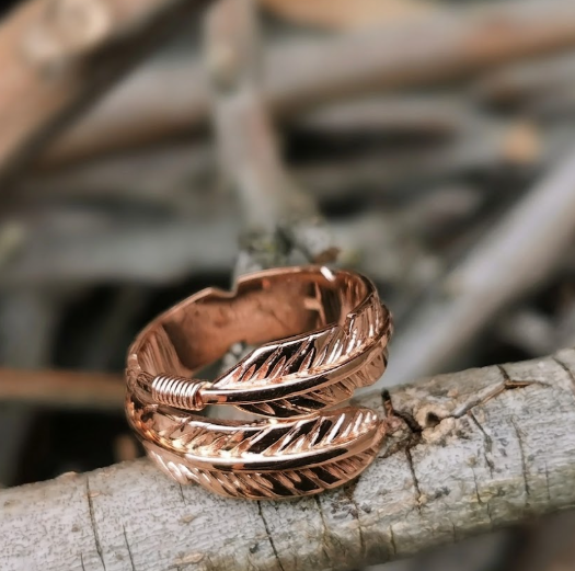 9ct rose gold large feather wrap ring with silver wire detail displayed on a weathered tree branch against a rustic wooden background.