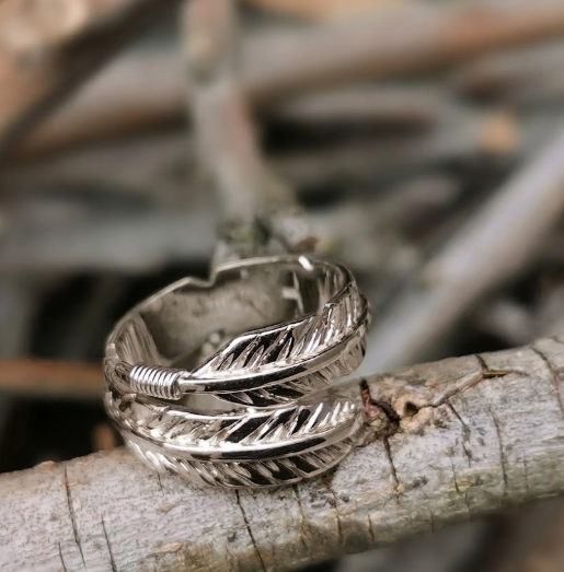 9ct white gold large feather wrap ring with silver wire detail resting on a weathered grey branch with a blurry wooden backdrop.