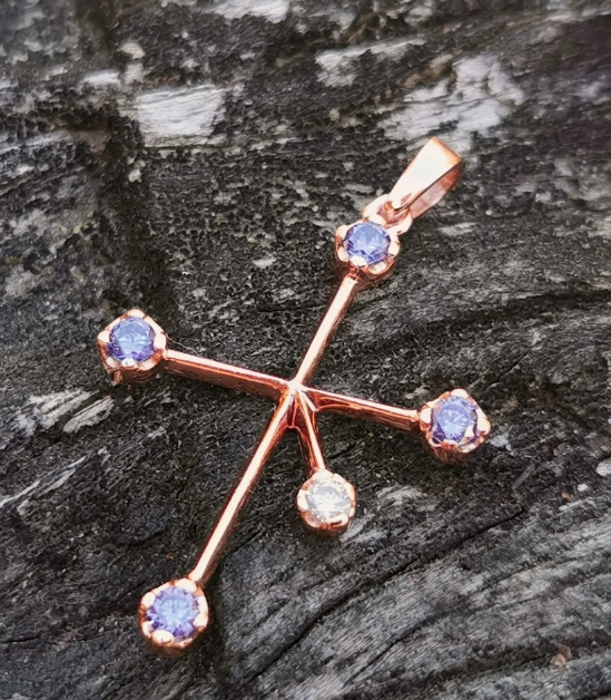 Close-up of a 9ct rose gold Southern Cross constellation pendant with four tanzanites and a diamond fifth star on dark weathered wood grain.