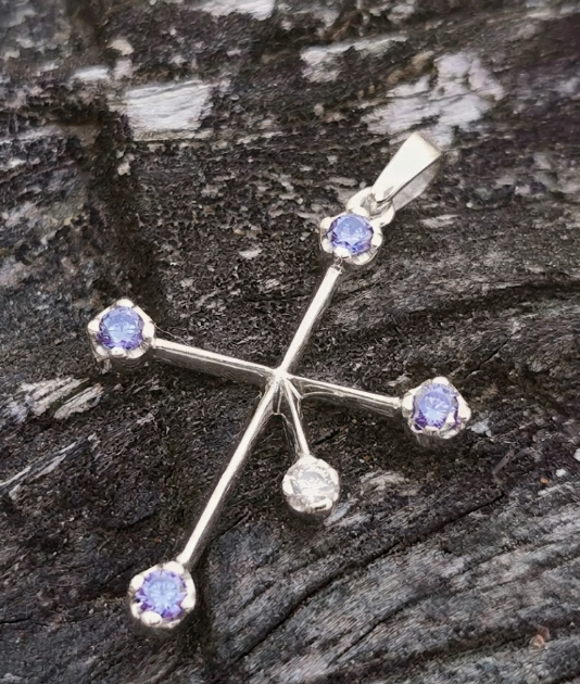 Close-up of a 9ct white gold Southern Cross constellation pendant set with four violet-blue tanzanite stars and a diamond fifth star on dark weathered wood.