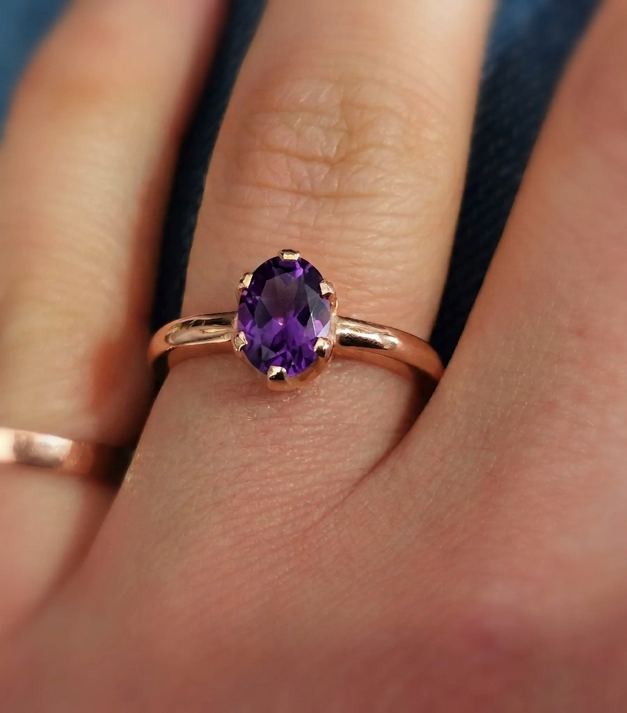 Close-up photograph of an oval-cut amethyst solitaire ring set in a traditional rose gold band.
