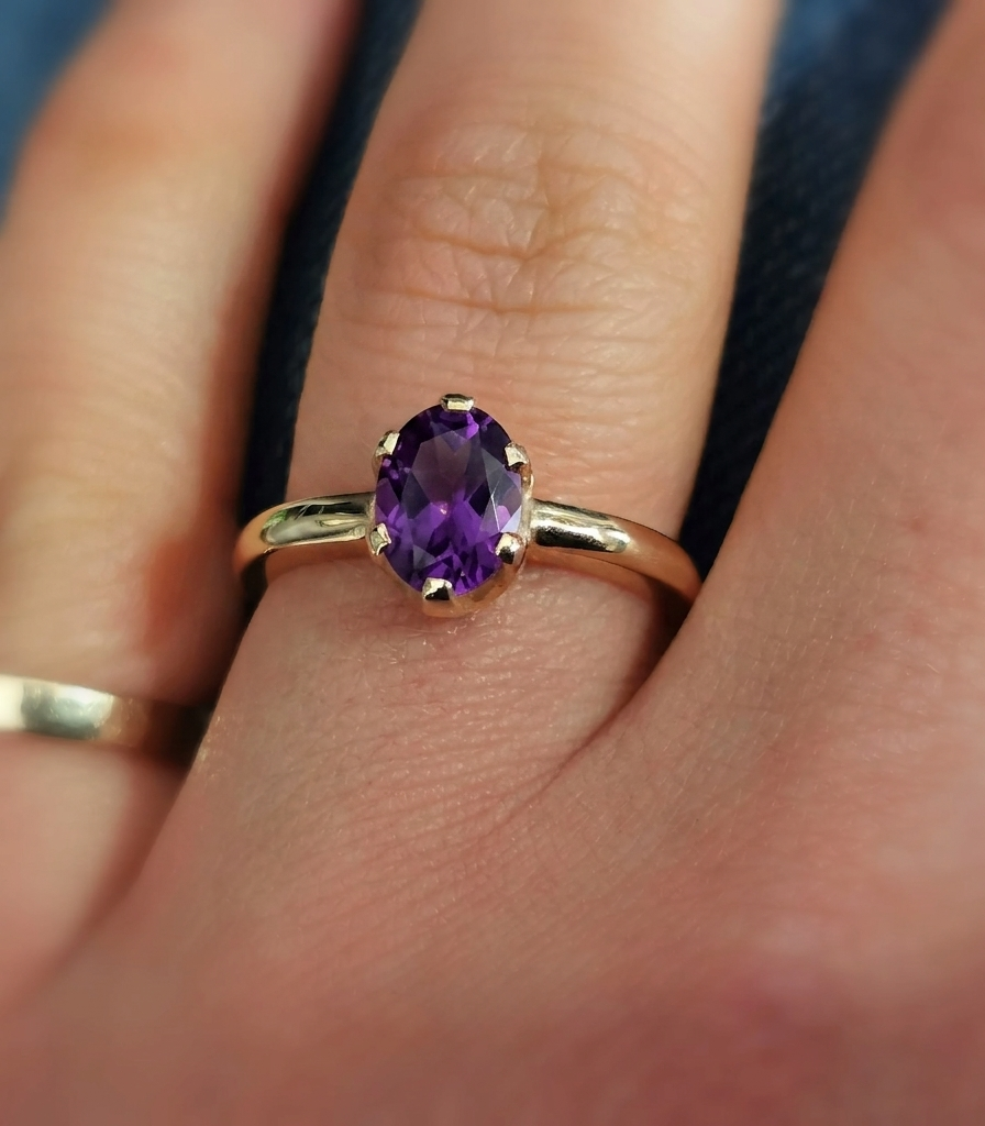 Close-up photograph of an oval-cut amethyst solitaire ring set in a traditional yellow gold band.