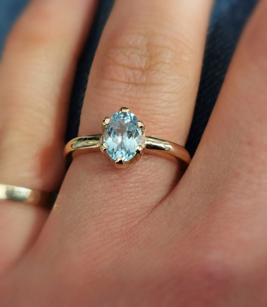Close-up photograph of an oval-cut icy blue aquamarine solitaire ring set in a polished yellow gold band