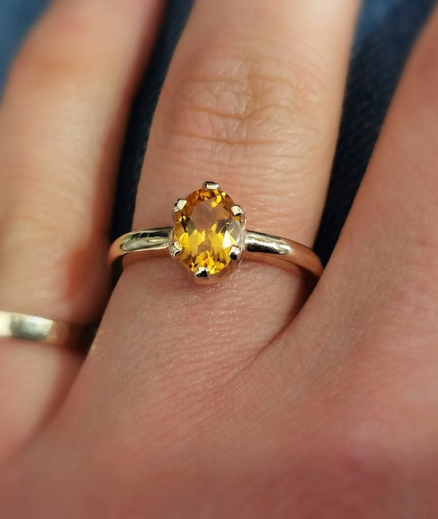 Close-up photograph of an oval-cut golden-yellow citrine solitaire ring set in a polished yellow gold band