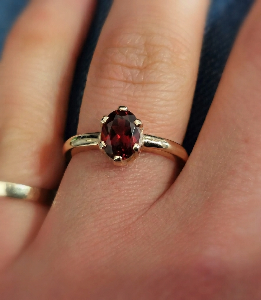 Close-up photograph of an oval-cut deep red garnet solitaire ring set in a polished yellow gold band