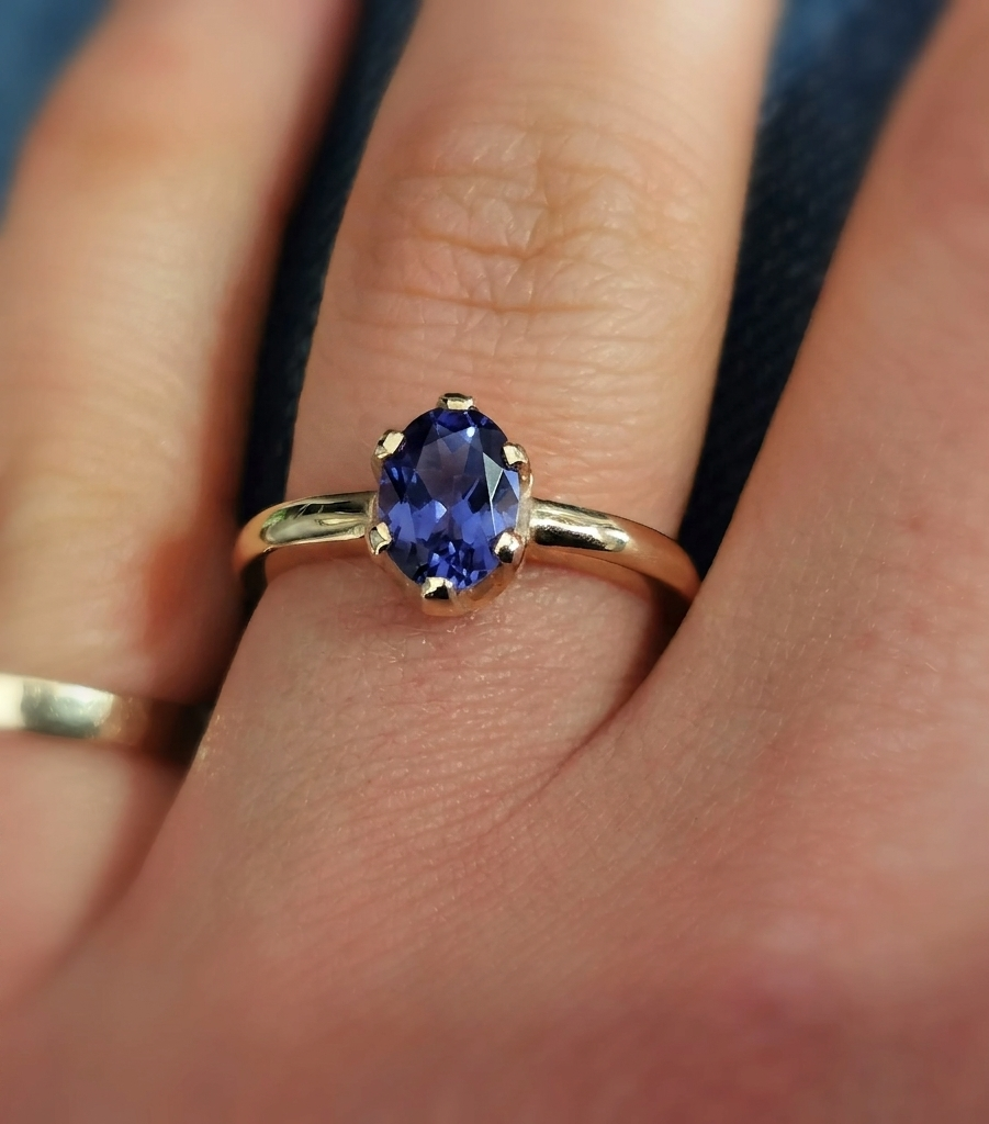 Close-up photograph of an oval-cut deep violet-blue iolite solitaire ring set in a polished yellow gold band