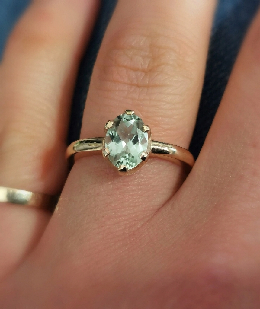 Close-up photograph of an oval-cut pale green prasiolite solitaire ring set in a polished yellow gold band
