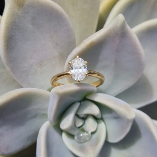 An oval-cut lab-grown diamond engagement ring with a classic claw setting on a 9ct yellow gold band